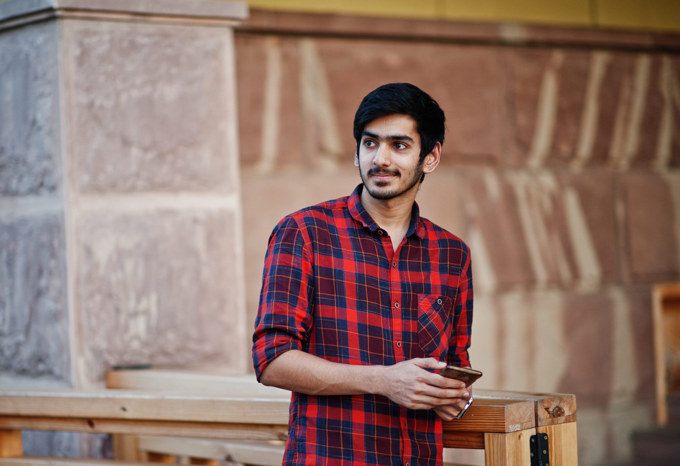 young indian student man red checkered shirt jeans posed city with mobile phone hands scaled e1775800448307